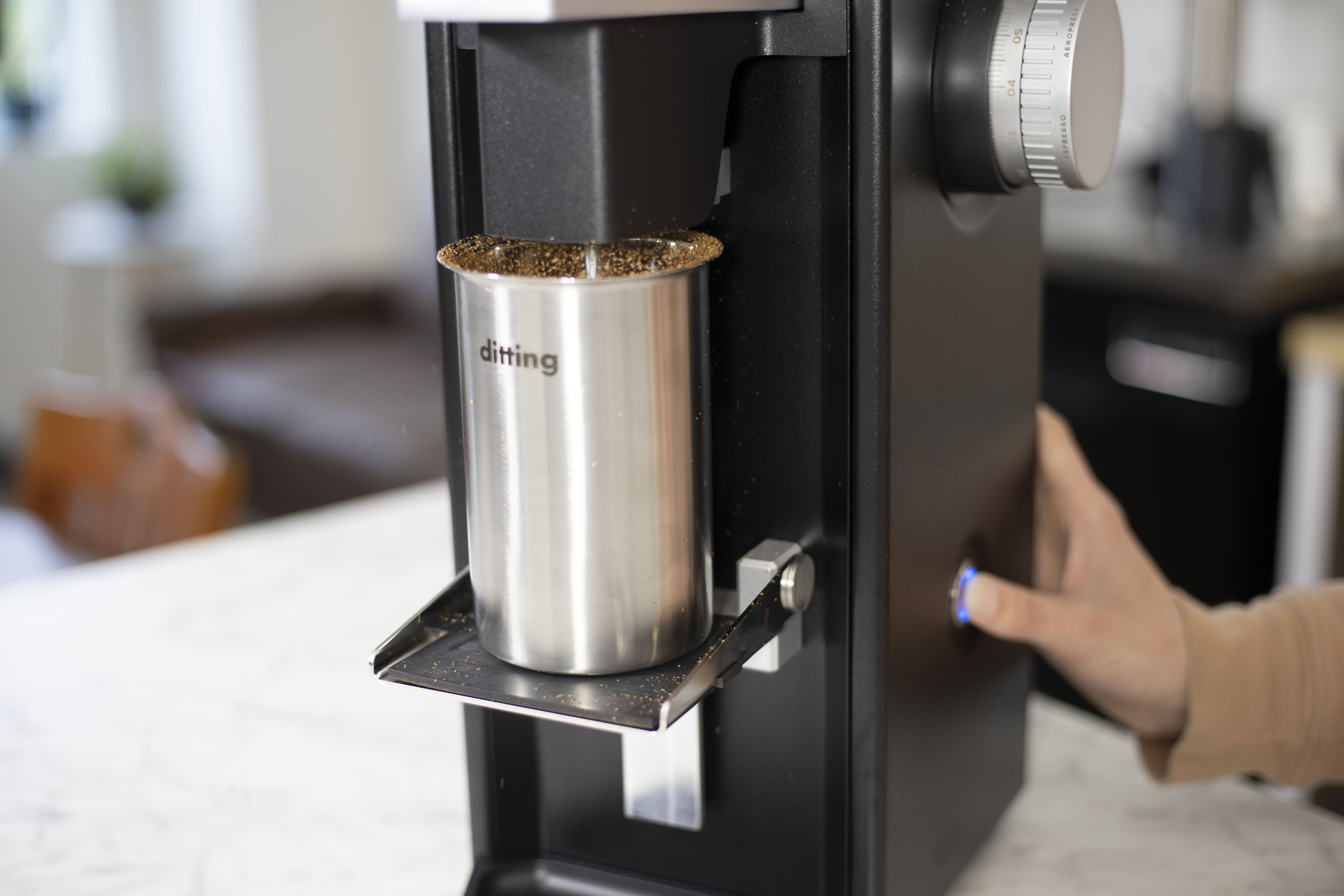 A hand turning on a Ditting Lab Sweet Coffee Grinder and Ditting grounds catch