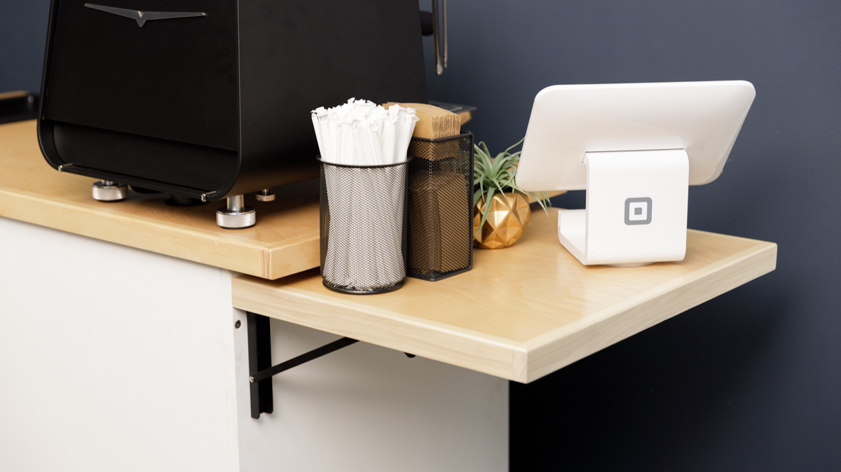 Side shelves on the Kickstart Coffee Cart with a POS system and straws on top of it.